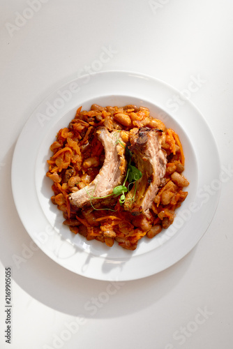 Fotografie Tender braised ribs sit atop a hearty bean and carrot stew on a clean white plate