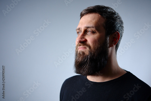 Fotografie A contemplative bearded man looks off-camera in a close-up profile portrait, showing full facial hair, calm expression and soft studio lighting, conveying introspection, maturity and quiet confidence
