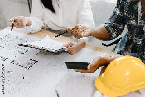 Canvastavla Blueprint Collaboration: Two individuals, one in a plaid shirt and the other in white, are engrossed in reviewing blueprints and discussing plans at a wooden table