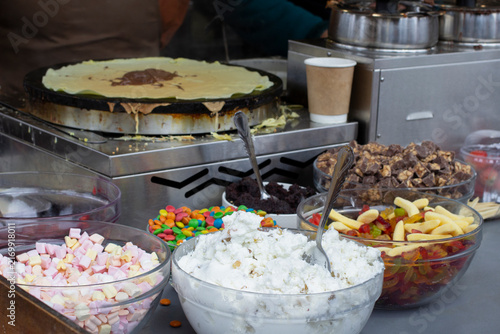 Pancakes on a frying pan and sweet fillings in bowls. Street food