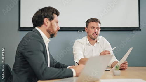 Two business professionals review documents and discuss project details. Collaboration is evident as insights are shared, fostering teamwork and strategic decision-making in corporate setting.