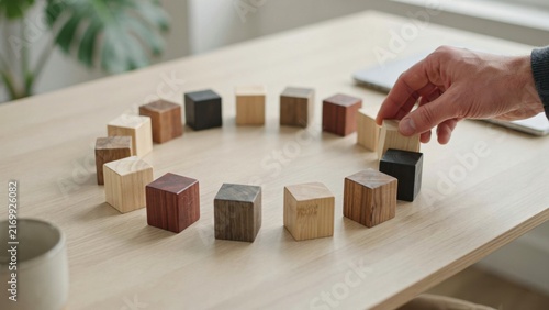 Hand arranging wooden cubes in circle structure for team unity and inclusive network concept.