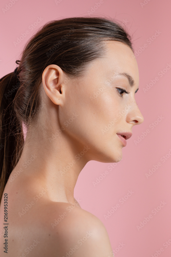 Fototapeta premium Profile of a young woman with smooth skin and subtle makeup on a pink background