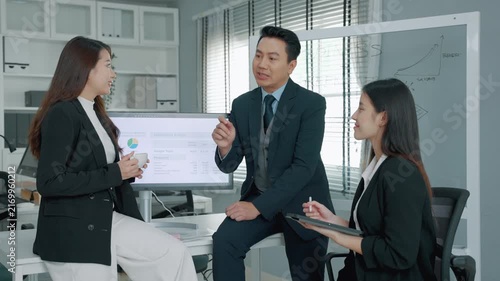 Business professionals having a strategic discussion in a modern office with a marketing budget presentation displayed on a monitor. Team members exchange ideas and evaluate business performance toget