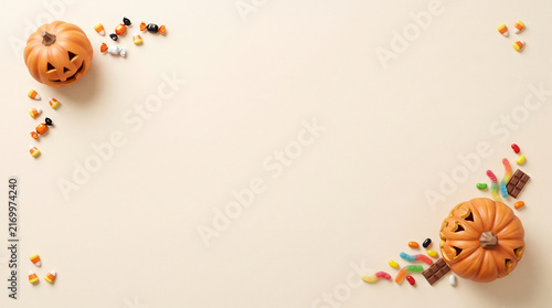 Halloween flat lay with carved pumpkins and colorful candy on a beige background