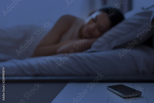 Fotografie Young Black woman sleeping in dark bedroom at night while smartphone resting on