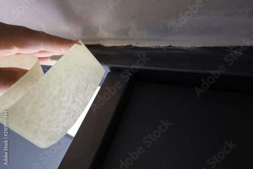 Konstfotografi A master hand applies paper masking tape to a wall corner near a dark door frame