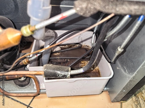 Foto ​Dirty refrigerator drain pan filled with stagnant water and mold behind the compressor and copper pipes during appliance maintenance