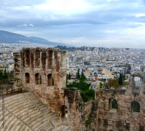 Historic stone ruins overlooking the dense urban cityscape of Athens, Greece, with mountains rising in the background.