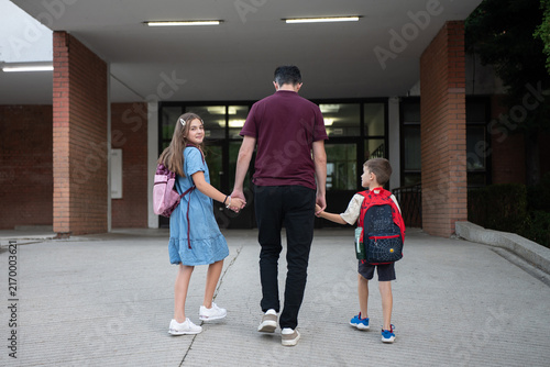 Back to school and education concept, father walking children to school holding hands with backpacks, family support and parental guidance for students.