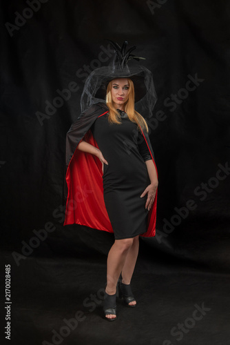 Fotografie Woman standing confidently in a black dress, a red lined black cape, and a witch