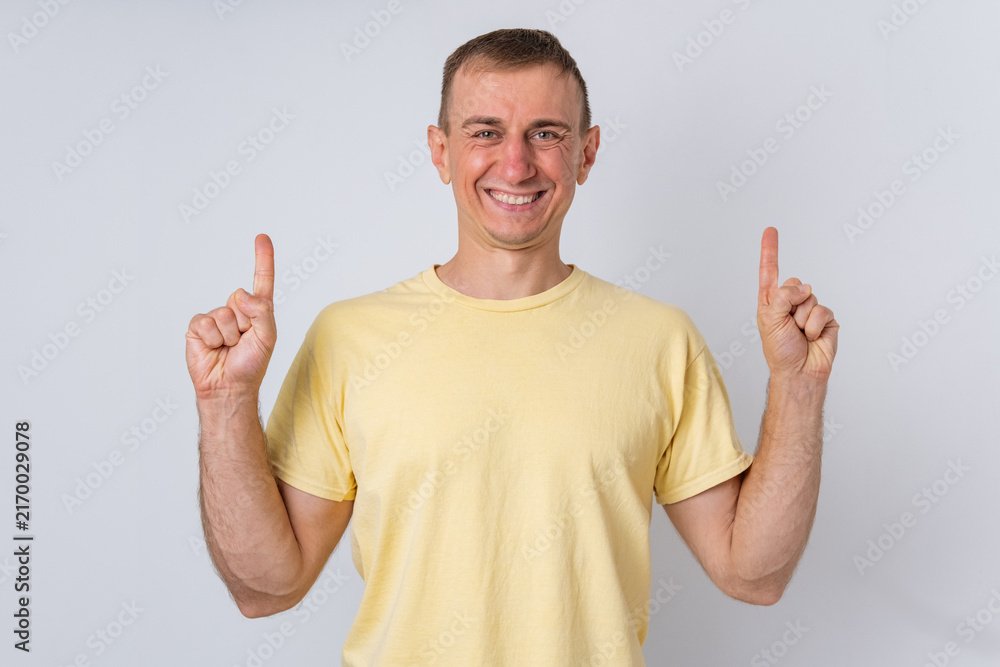 Fototapeta premium Smiling man pointing both index fingers upwards, indicating ample copy space above for advertising messages, promotions, or important information on a clear background