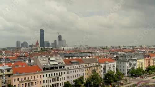Vienna's skyline with historic residential buildings, orange tile roofs, and modern skyscrapers. Overcast sky with clouds over Austrian capital cityscape.