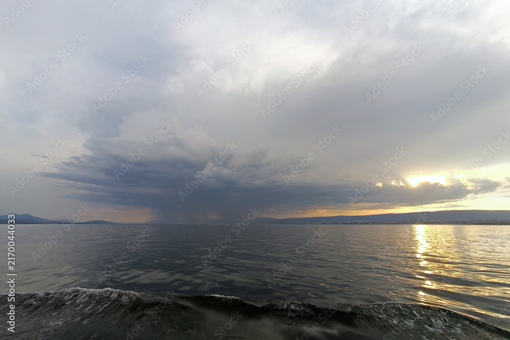 Fototapeta premium Dramatic Storm Clouds and Rain over Lake at Sunset with Golden Reflection on Water
