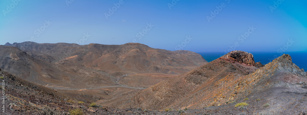 Obraz premium Panoramic view of arid volcanic mountains and coastal cliffs overlooking Atlantic Ocean in Fuerteventura, Canary Islands.
