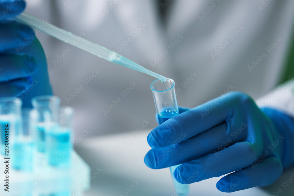 Fototapeta premium Laboratory worker dripping liquid into test tube at white table indoors, closeup