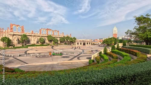 Wide view of a large, well-maintained alley in central Fukuoka, Vietnam, featuring patterned tiles, a Roman-style mini amphitheater, palm bushes, trees, and a clock tower.
