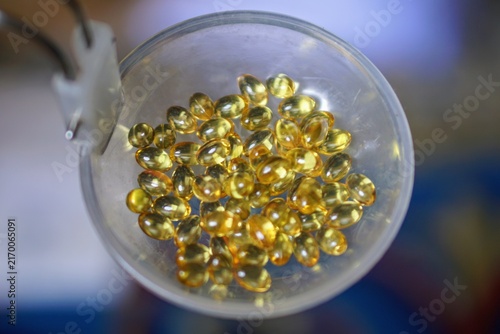High angle shot of clear gel capsule vitamin supplements collected in a small transparent container.