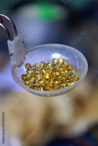High angle shot of clear gel capsule vitamin supplements collected in a small transparent container.