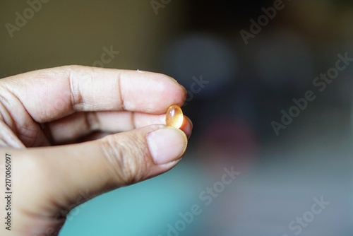 Close-up of human fingers holding a single transparent golden yellow fish oil softgel capsule.