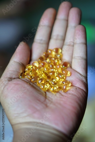 Close-up of a human hand holding a pile of golden yellow softgel fish oil capsules.