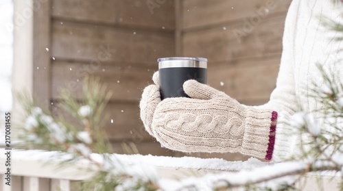 Person in Warm Knitted Mittens Holding a Black Thermal Travel Tumbler Outdoors on a Snowy Winter Day