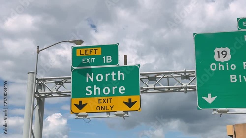 Highway sign directs motorists toward Pittsburgh's North Shore at Exit 1B beneath a cloudy sky, representing urban travel and transportation. 15322  