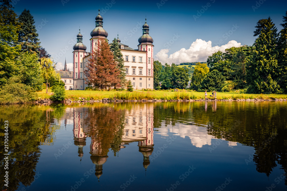 Naklejka premium Vrchlabsky castle reflected in the calm waters of old pond. Sunny summer cityscape of Vrchlabi town, Trutnov District, Hradec Kralove Region of Czech Republic, Europe. Traveling concept background.