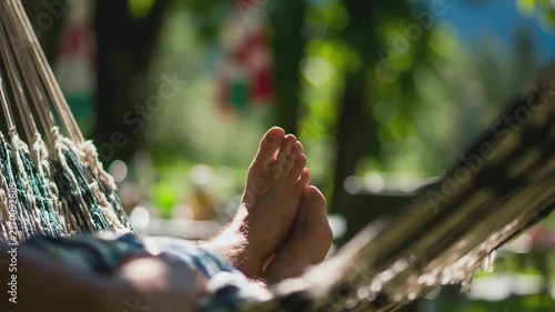 Summer hot vibe lifestyle. A closeup shot of a persons bare feet resting in a hammock. The person wears a blue and white patterned shirt.