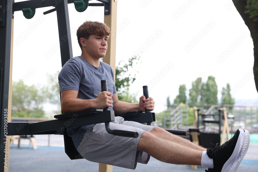 Fototapeta premium Teenage boy exercising on dip station at outdoor sports ground. Space for text