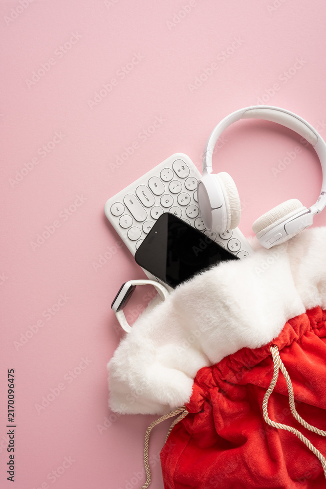 Naklejka premium Santa present bag with headphones, keyboard and smartwatch for Merry Christmas and Happy New Year on vertical pastel pink background