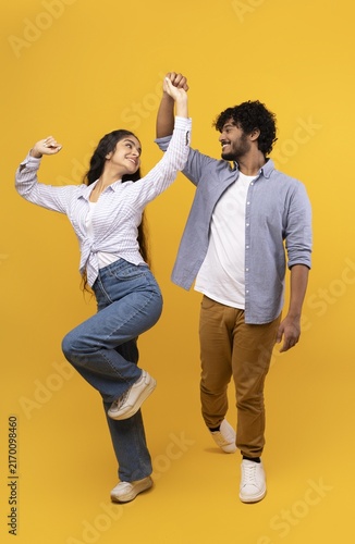 Фотография Smiling Young Hispanic Couple Engaging In Dance At Studio, Joyful Emotion Reflecting Happiness, Full-body Shot With Yellow Background, Fun Activity, Lifestyle Concept