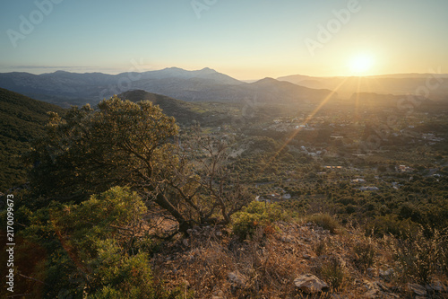 Принти на полотні Sunset viewed across scrub-covered hills toward a populated Sardinian valley and distant mountain ridges glowing in warm evening light