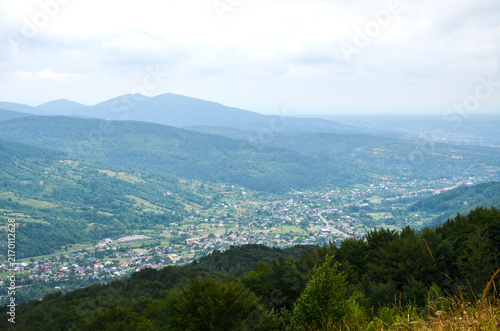 Panoramic view of a lush mountain valley with a Yaremche village nestled among forested hills and winding roads under an overcast sky. Carpathian Mountains, Ukraine