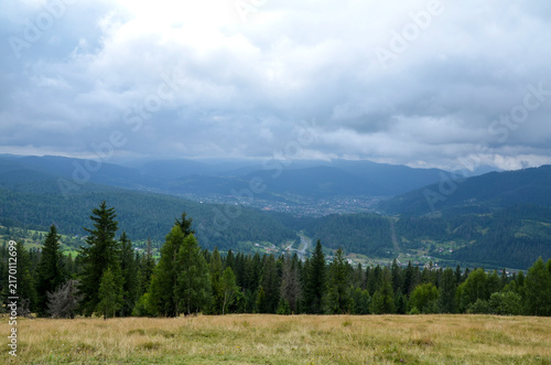 Panoramic view of a lush mountain valley with a Yaremche village nestled among forested hills and winding roads under an overcast sky. Carpathian Mountains, Ukraine