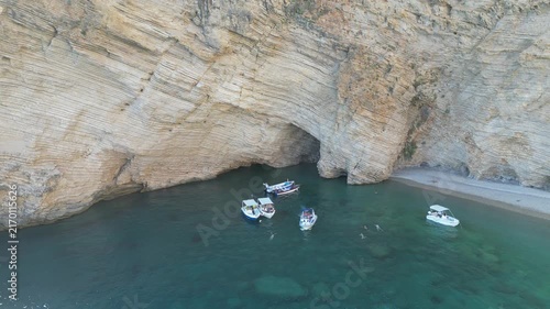 Aerial fly‑away from boats showing turquoise water and limestone cliffs at Chomi Beach in Corfu near Paleokastritsa