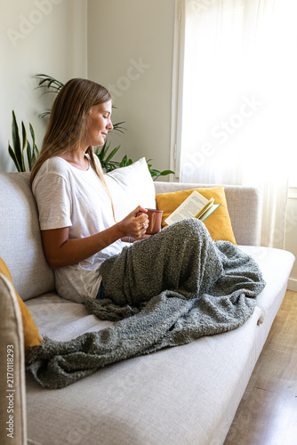 Female relaxing at home reading book enjoying herbal tea. Vertical.
