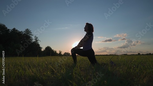 A woman practices sport in the park during sunset. The park provides a calm setting for the sport, highlighting the woman's focus on her workout in nature.
