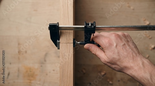 Hand tightening a metal clamp on wooden boards in a workshop