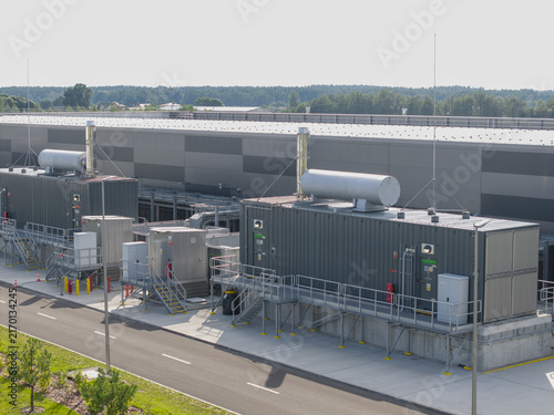 Aerial view of ai data center power generator system with industrial containers and cooling units installed next to a large warehouse facility in Poland.