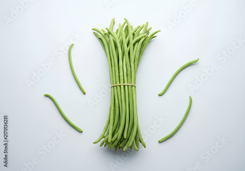 Top view of a bundle of fresh raw yardlong beans or kacang panjang tied together on a light grey surface.