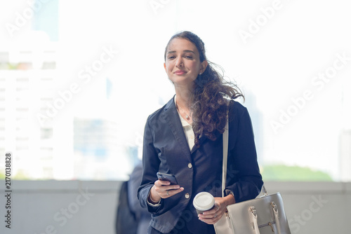 Fotografie A smiling Hispanic businesswoman in a dark suit using a mobile phone between app
