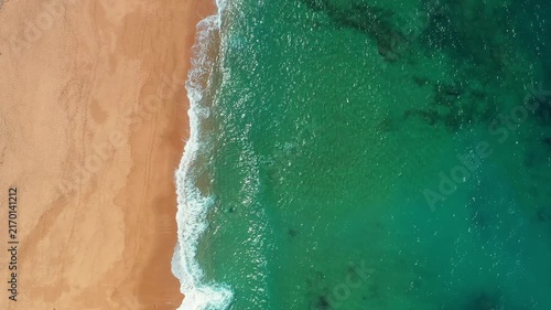 Drone view from above of emerald Atlantic water and breaking waves reaching an empty sandy beach in Portugal.
