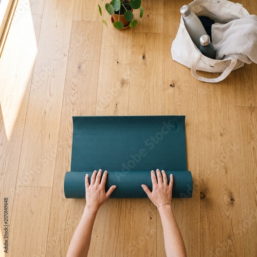 Hands unrolling green yoga mat on wooden floor in bright minimalist home interior with natural light