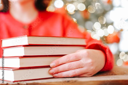 Holiday Reading Books.Woman Reading Books During Christmas Winter Holidays.hardcover books beside a glowing Christmas tree for bookstore advertising, library events, winter reading 