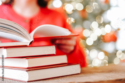 Christmas reading.Christmas books. Woman Turning Pages of a Book by Christmas Tree Lights for holiday reading lists,book clubs,winter leisure and educational content. 