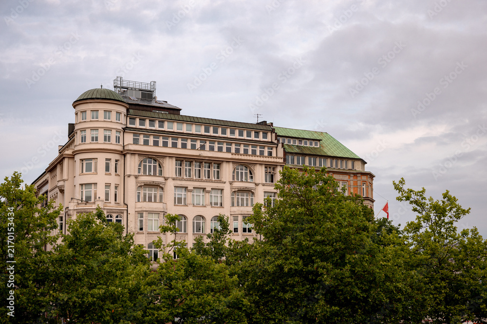 Obraz premium Hamburg, Germany - July 1, 2026: Historic architecture partly obscured by trees in central Hamburg, Germany.