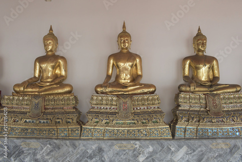 фотографія three golden buddha statues seated on richly decorated traditional pedestals