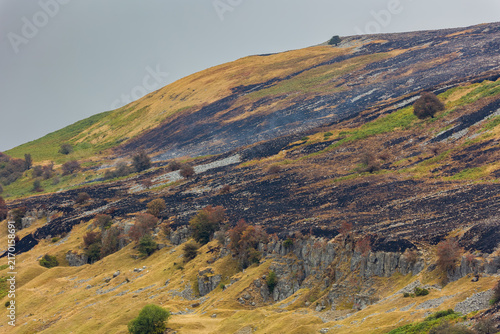 Obraz na płótnie Burnt moorland vegetation covering steep hillside above limestone crags, smoke d