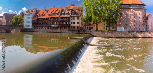 Obraz na plátně Traditional riverside buildings reflected in the Pegnitz River beside a weir on a sunny summer day in Nuremberg, Germany